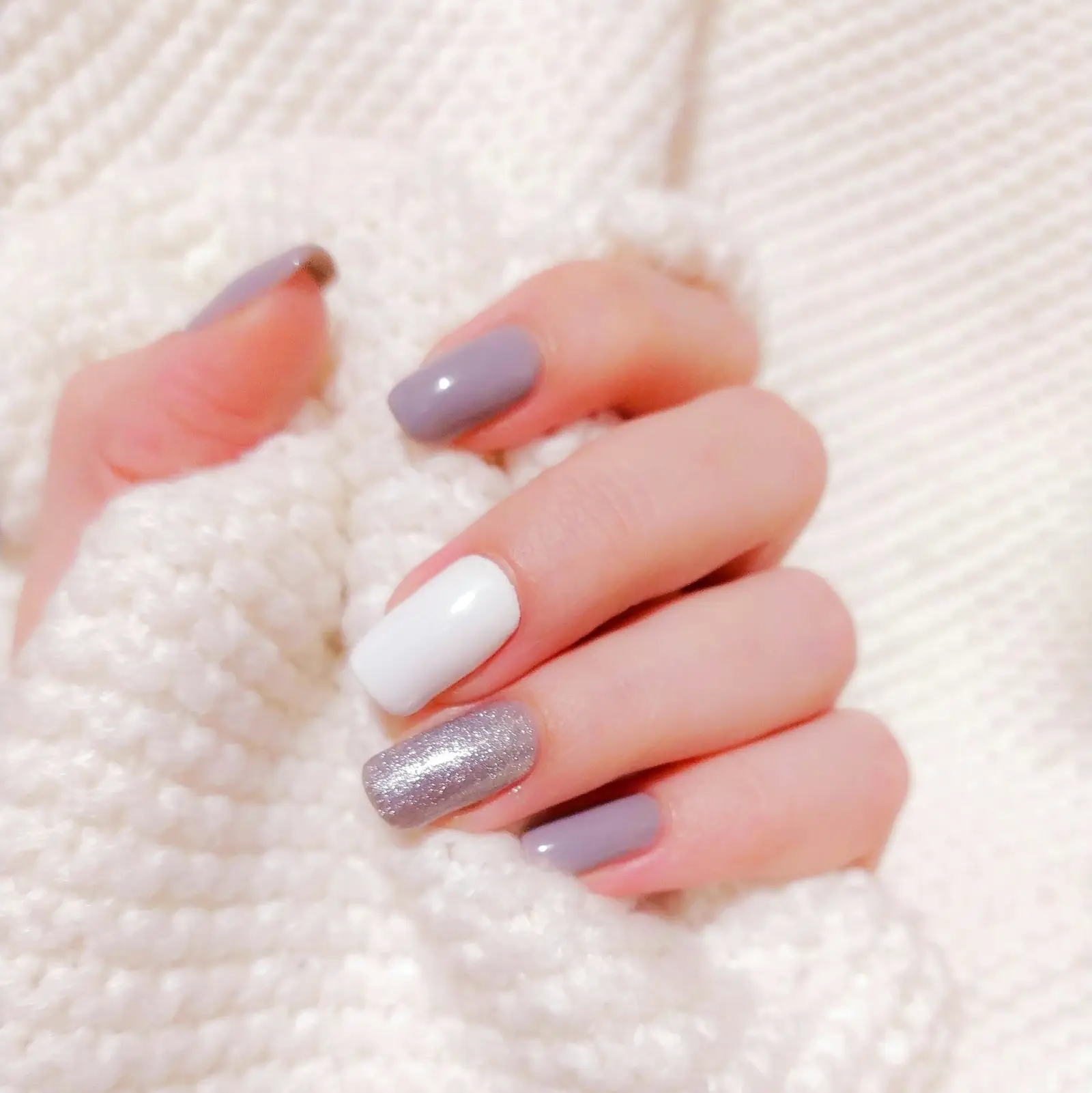 Mauve, white and silver glitter nails against a knit sweater