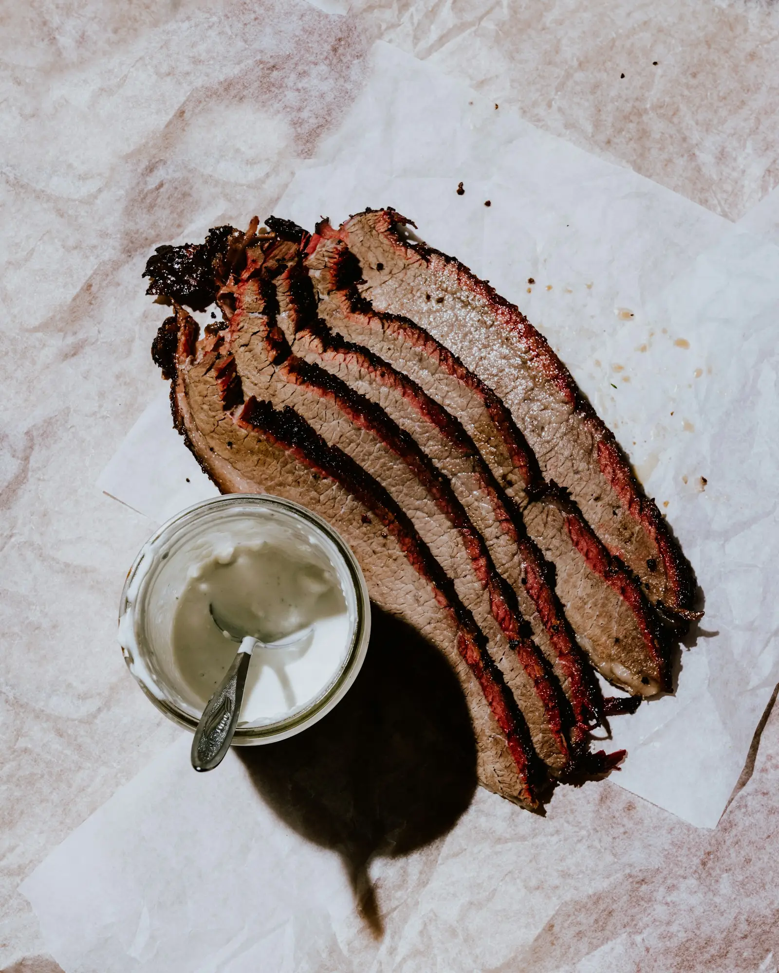Brisket slices fanned out next to a cup of white sauce
