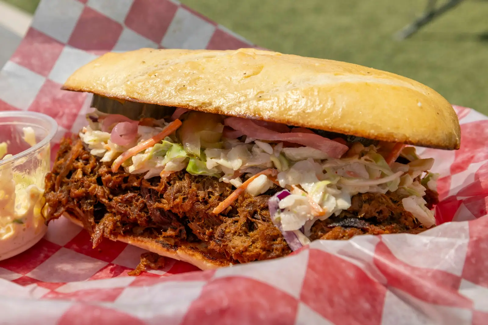 Pulled pork sandwich with slaw and pickles on checkered paper