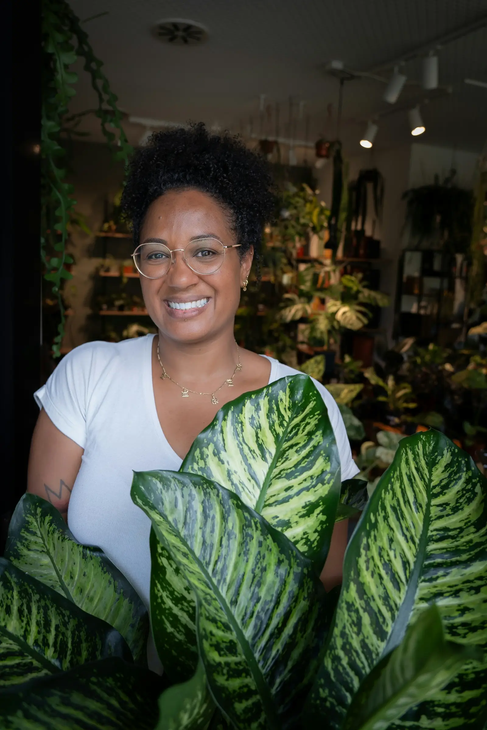 A smiling shop owner holding a large leafy plant inside the shop
